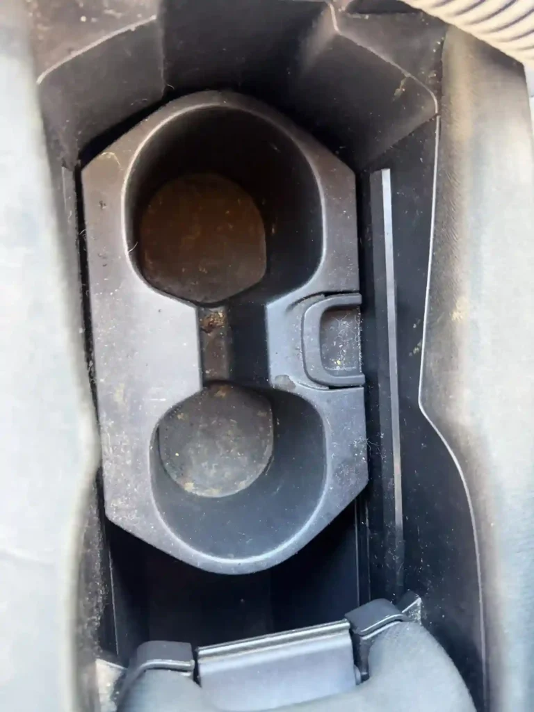 Grimy dual cup holders in a car's center console before professional detailing 