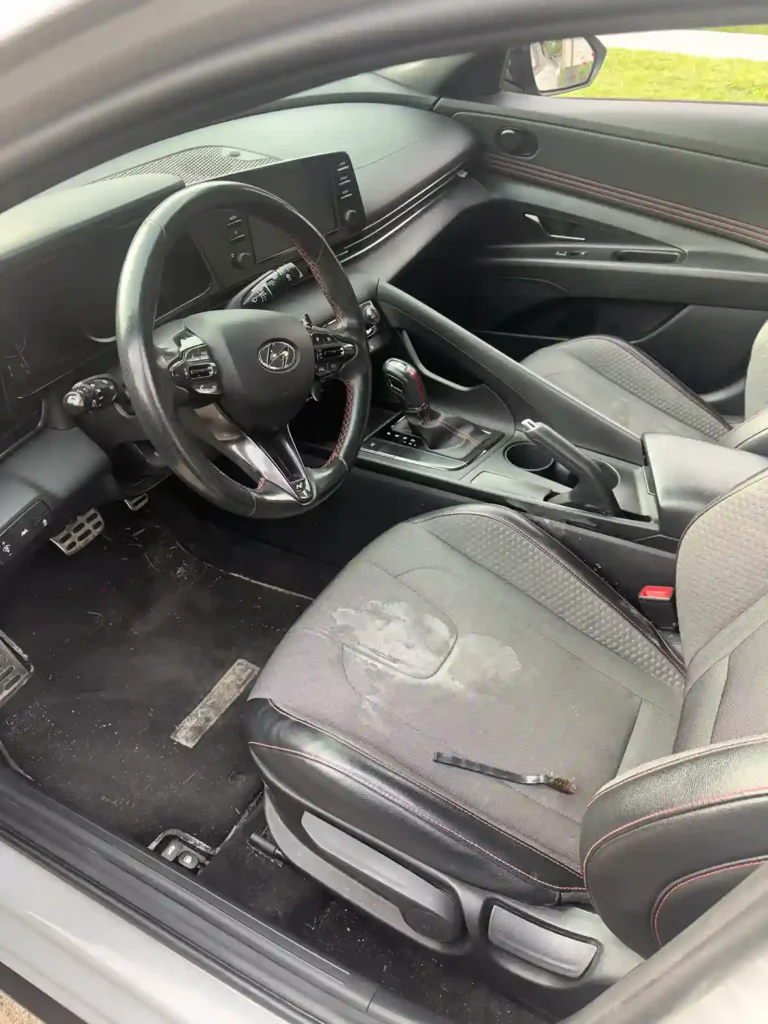 Front car seat with a visible stain and dusty footwell before cleaning 