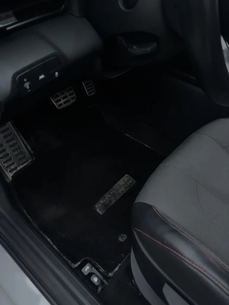 Dimly lit rear floor mat and footwell area inside a car's dark interior 