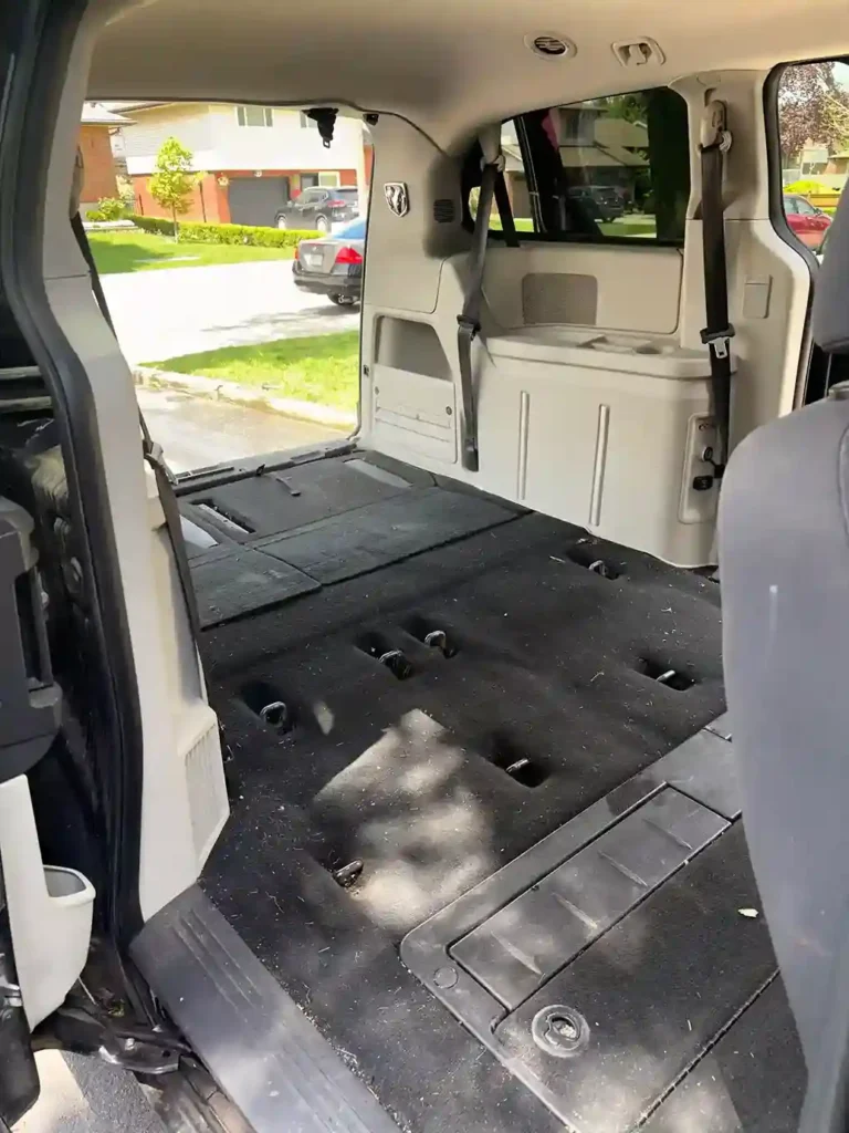 Empty minivan cargo area with folded seats and dusty carpet before detailing 