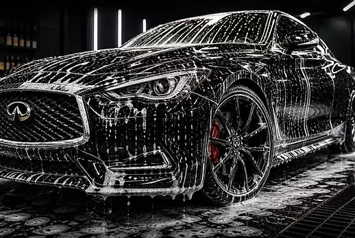 Black Infiniti Q60 covered in thick snow foam during a premium exterior wash under dramatic lighting