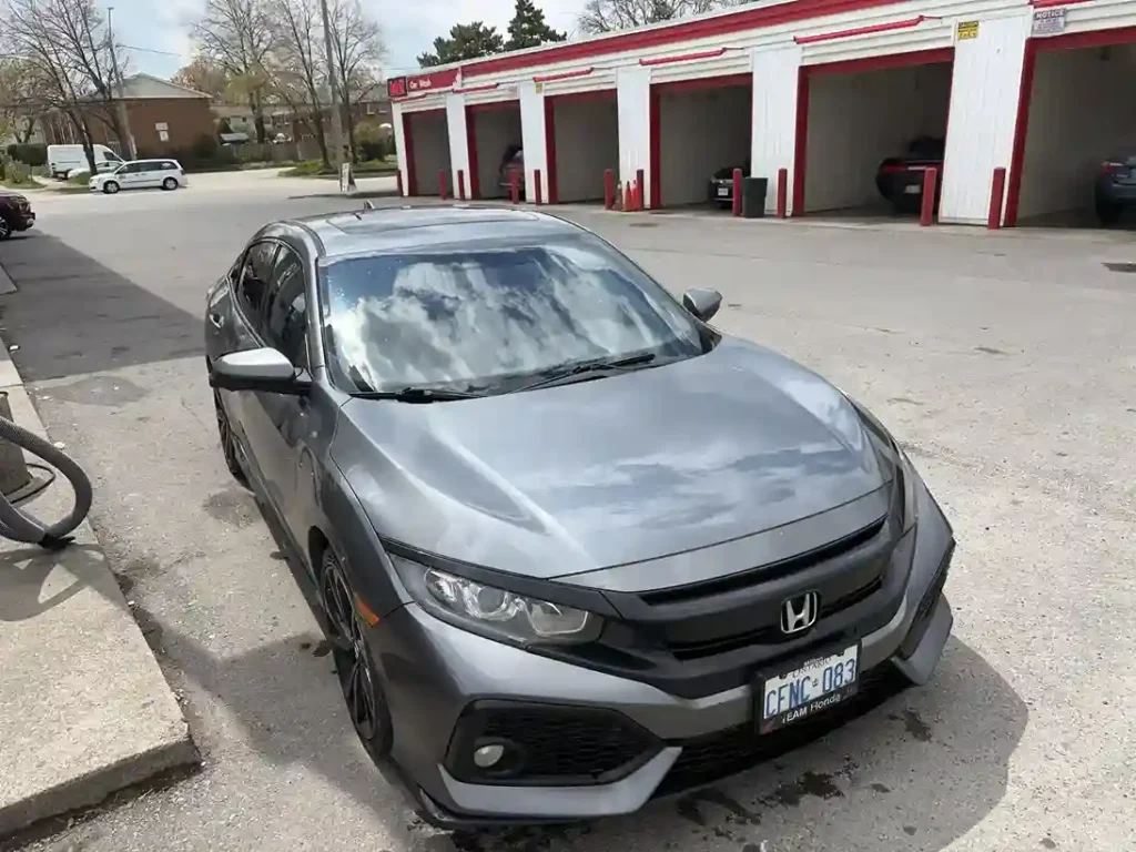 Gray sedan with a glossy, freshly detailed exterior parked at a car wash 