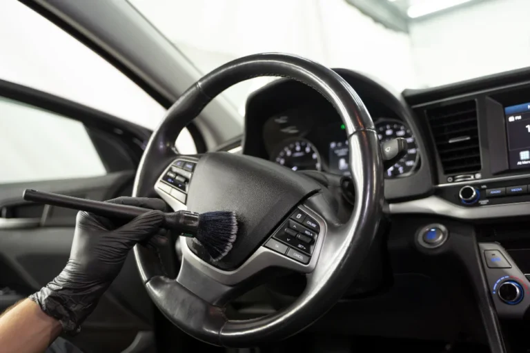 Detailer dusting the center of a steering wheel using a soft makeup-style detailing brush