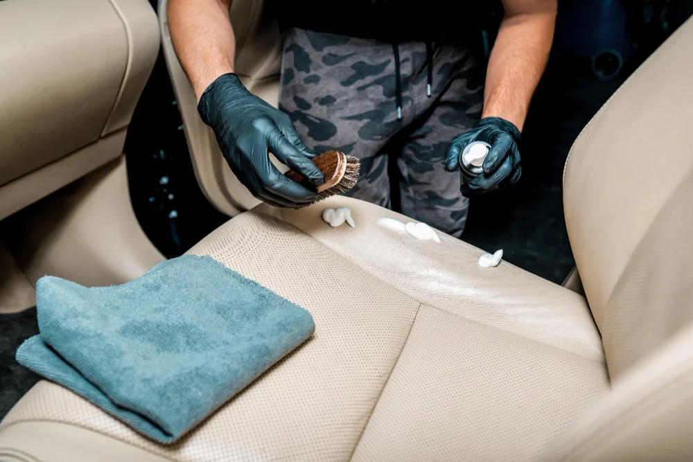 Detailer wearing black gloves scrubbing foam cleaner into a car seat with a brush in Hamilton