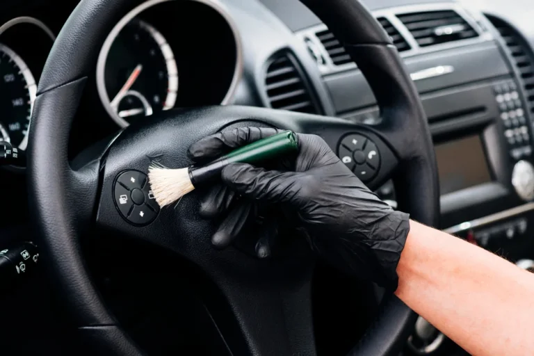Detailer at pure detailing wearing black gloves using a small soft brush to clean steering wheel controls