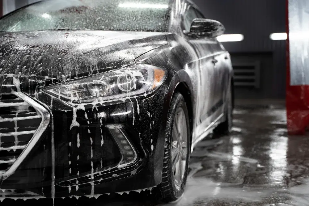 Black vehicle covered in thick active soap foam during a pre-wash soak, pure detailing